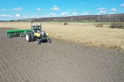 Tractor pulling a grain drill across dark spring soil