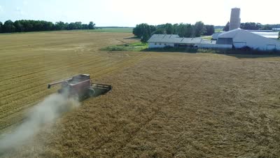 Aerial still of the combine in golden barley with the farmstead beyond