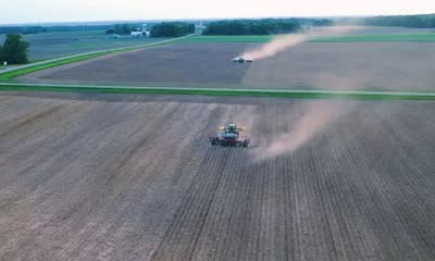 Aerial dusk view of two tractors working fields, dust trailing