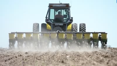 Rear view of a planter raising dust across a dry spring field